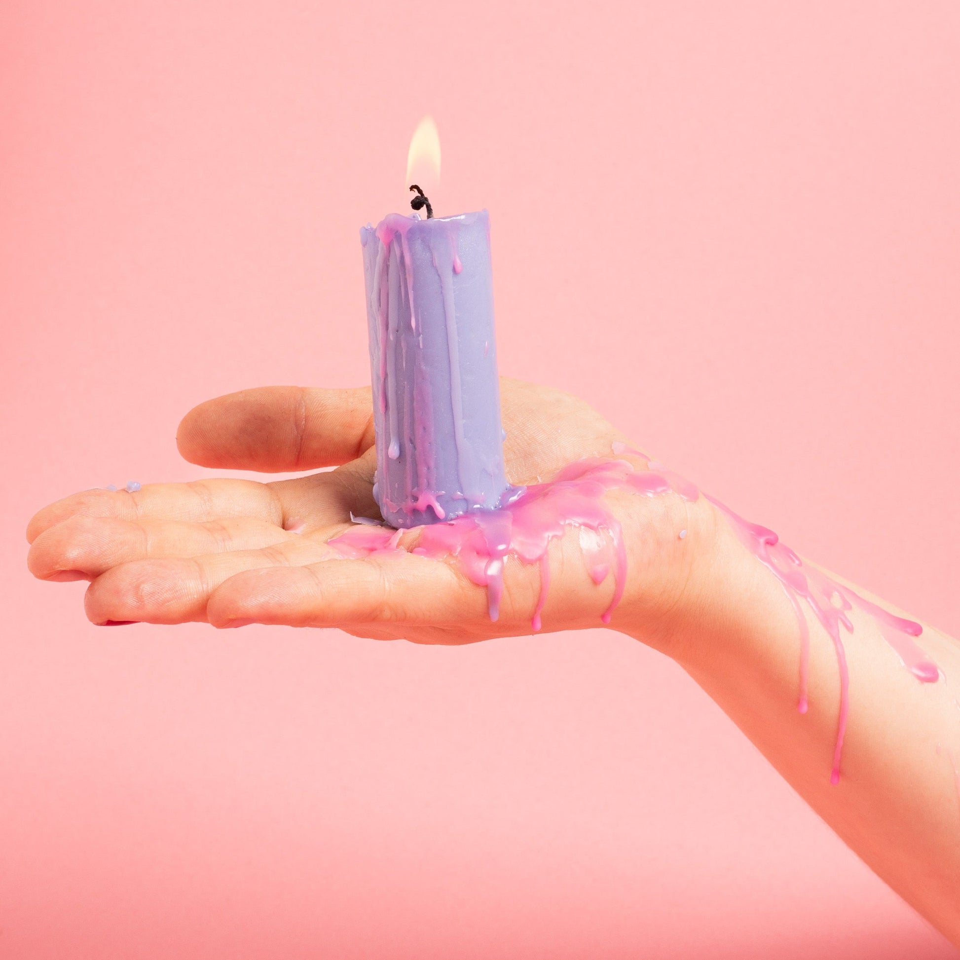 Vahakynttilä kädessä vaaleanpunaisella taustalla, vahaa valuu pitkin kättä