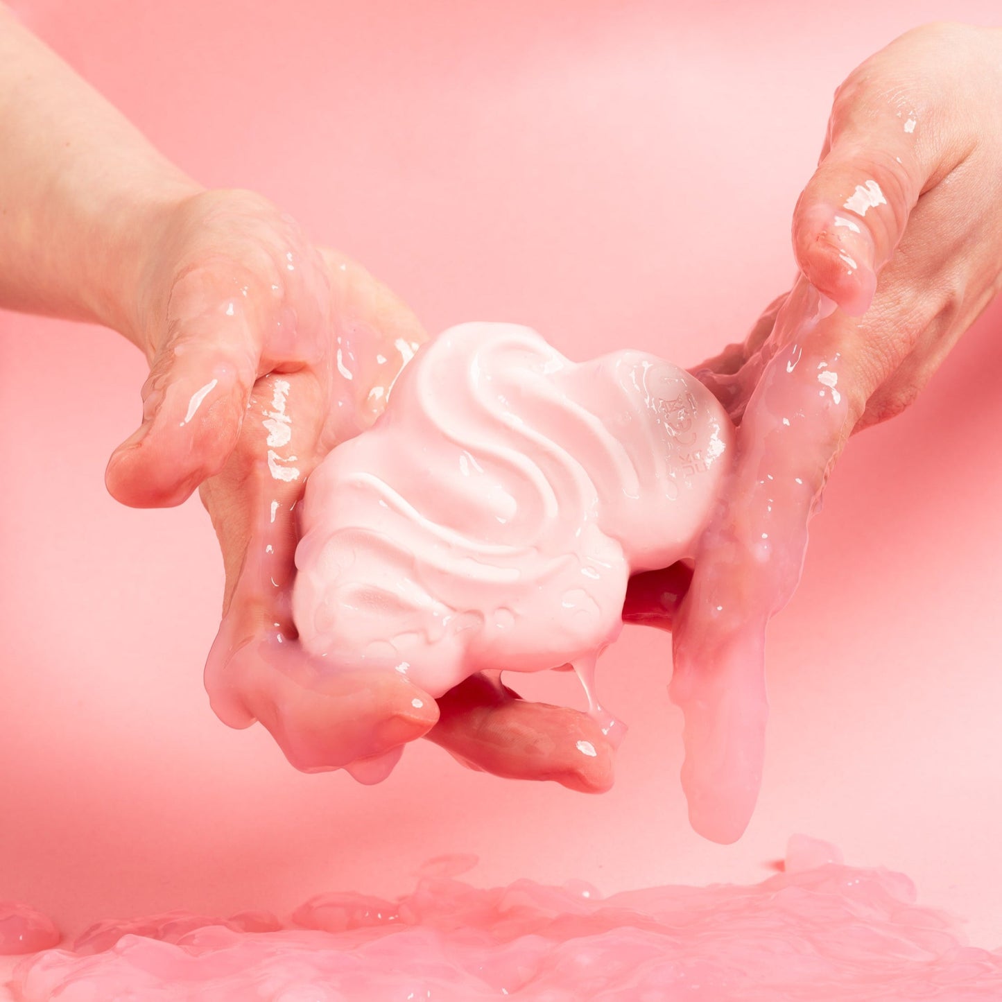 Pilvi vibraattoria pidetään kahdella kädellä vaaleanpunaista taustaa vasten.